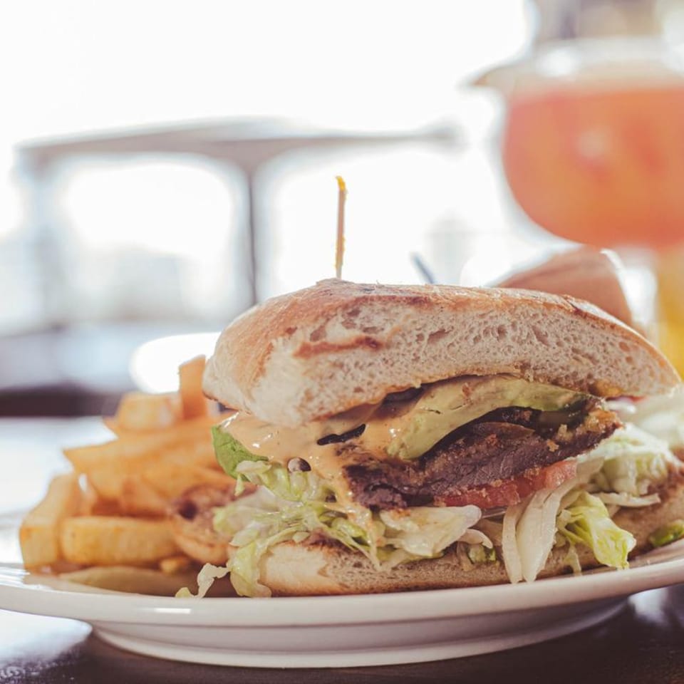 A Mexican torta sandwich with avocado, lettuce, and sauce, served with a side of fries.