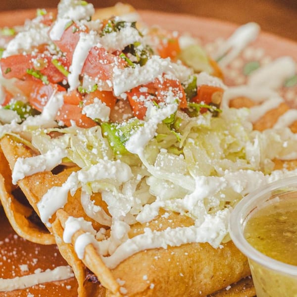 Crispy LA Taco Cantina flautas topped with shredded lettuce, diced tomatoes, cotija cheese, and crema.