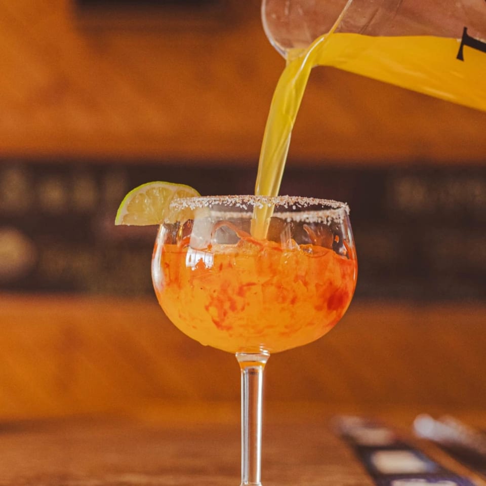 Bright yellow liquid pours into a margarita glass with a lime wedge and salted rim.