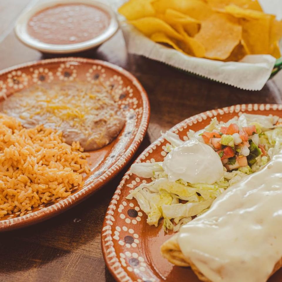 Mexican meal with rice, beans, a burrito, salsa, and tortilla chips on a wooden table.